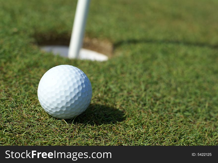 Golfball in front of the hole in green grass