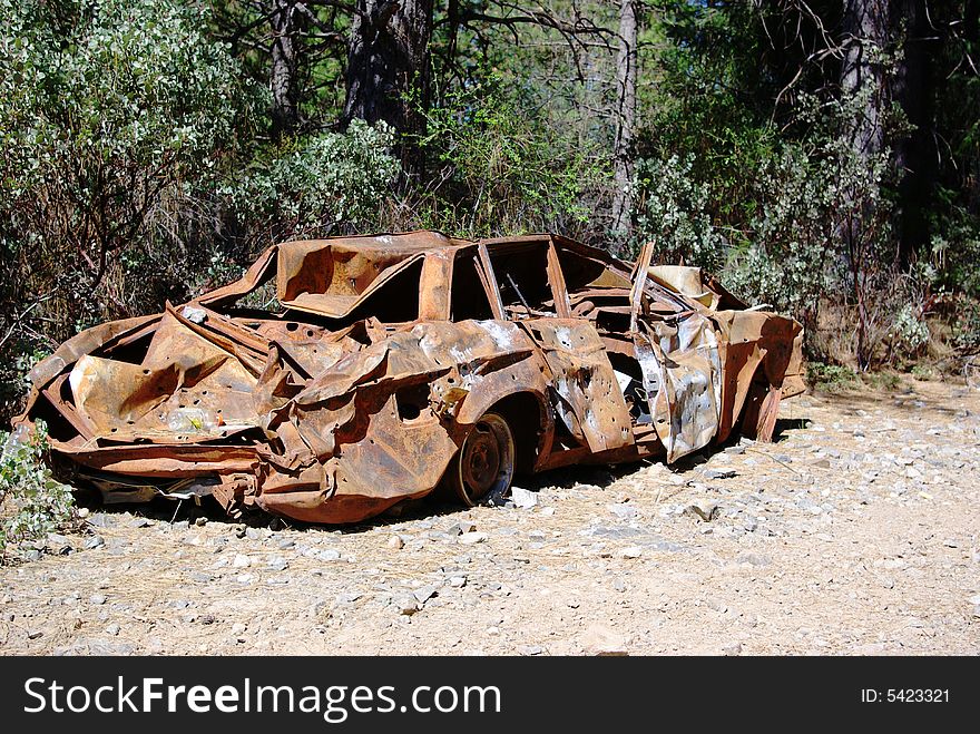 An abandoned old car with bullet holes, crushed and rusty  from being burnt parked in the forest. An abandoned old car with bullet holes, crushed and rusty  from being burnt parked in the forest.