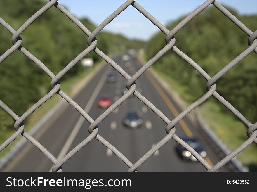 Close-up view of fence with highway below on background. Close-up view of fence with highway below on background