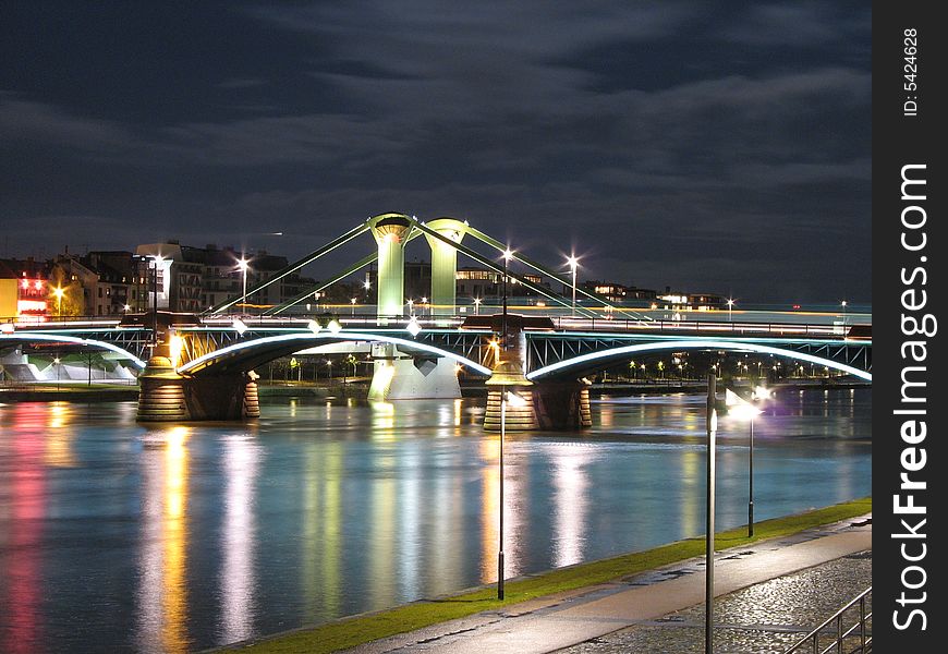 A bridge over a river lit up at nigh by a number of lights. A bridge over a river lit up at nigh by a number of lights