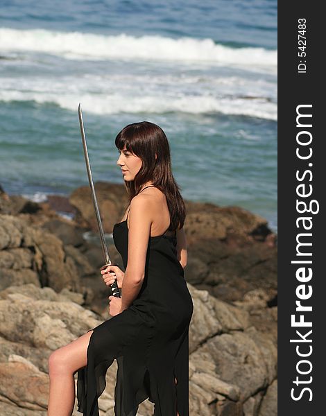 A beautiful white caucasian woman holding a sword on the beach. A beautiful white caucasian woman holding a sword on the beach