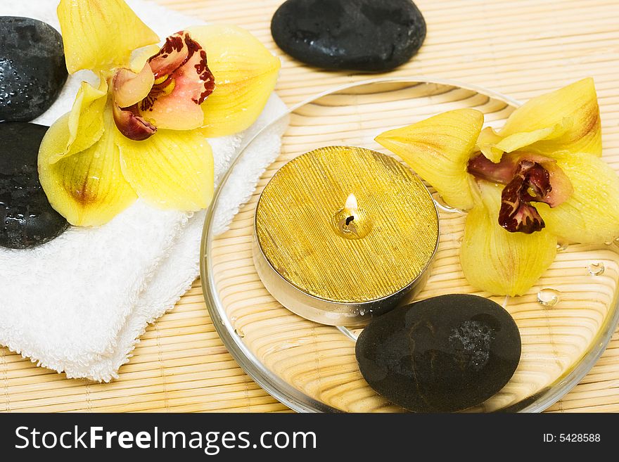Candle in water with yellow orchids and towel