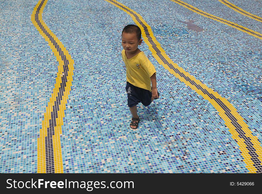 A little Chinese boy running happily on the mosaic ground of a swimming pool. A little Chinese boy running happily on the mosaic ground of a swimming pool.