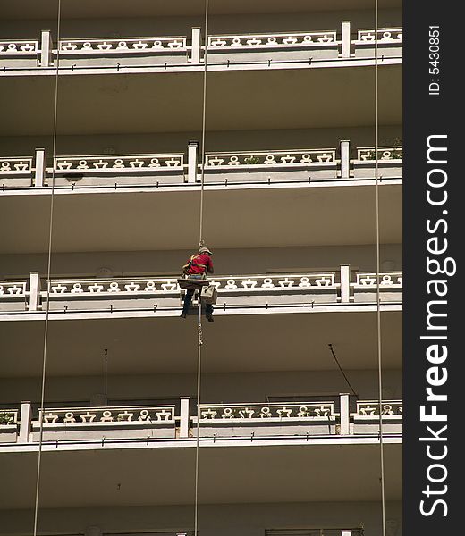Man hanging at a facade of a house with balconies is cleaning the railings. Man hanging at a facade of a house with balconies is cleaning the railings