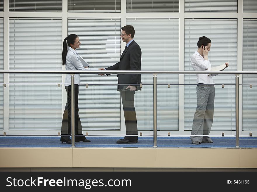 Businessman and businesswoman shaking hands on modern office corridor. three persons. Businessman and businesswoman shaking hands on modern office corridor. three persons