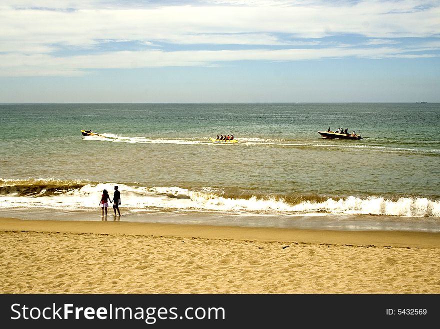 Sailing boats at sea and a couple walking along the beach at Puerto Vallarta, Mexico