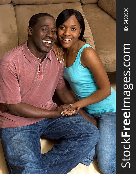 Happy, attractive, couple sitting on the floor in front of a couch. They are smiling and holding hands. Vertically framed photograph. Happy, attractive, couple sitting on the floor in front of a couch. They are smiling and holding hands. Vertically framed photograph