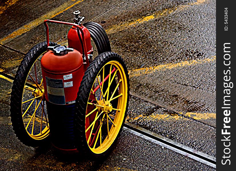 Fire Extinguisher on Wheels parked on the pavement with yellow lines. The photo has an antiquated essance look and feel to it.