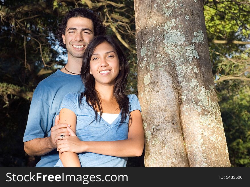 A Happy couple embraces in front of a tree. Horizontally framed photograph. A Happy couple embraces in front of a tree. Horizontally framed photograph.