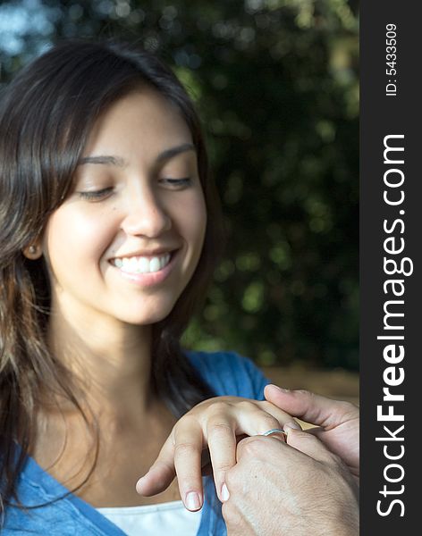 A woman smiles as someone slips an engagement ring upon her finger. Vertically framed photograph. A woman smiles as someone slips an engagement ring upon her finger. Vertically framed photograph.