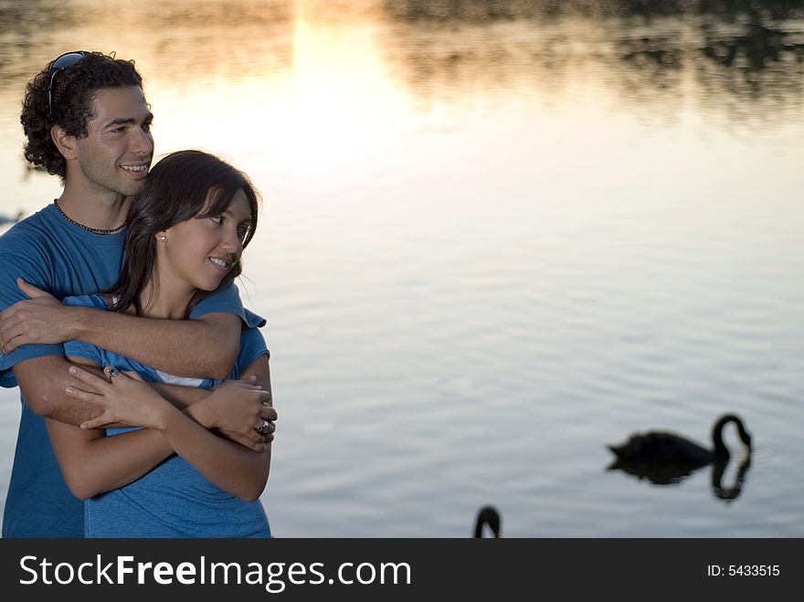 A Happy couple embraces in front of a beautiful pond with swans swimming in it. Horizontally framed photograph. A Happy couple embraces in front of a beautiful pond with swans swimming in it. Horizontally framed photograph.