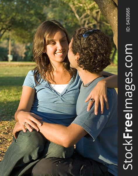 Happy, couple sit in the woods. She sits on his lap a they look at each other and smile. Vertically framed photograph. Happy, couple sit in the woods. She sits on his lap a they look at each other and smile. Vertically framed photograph