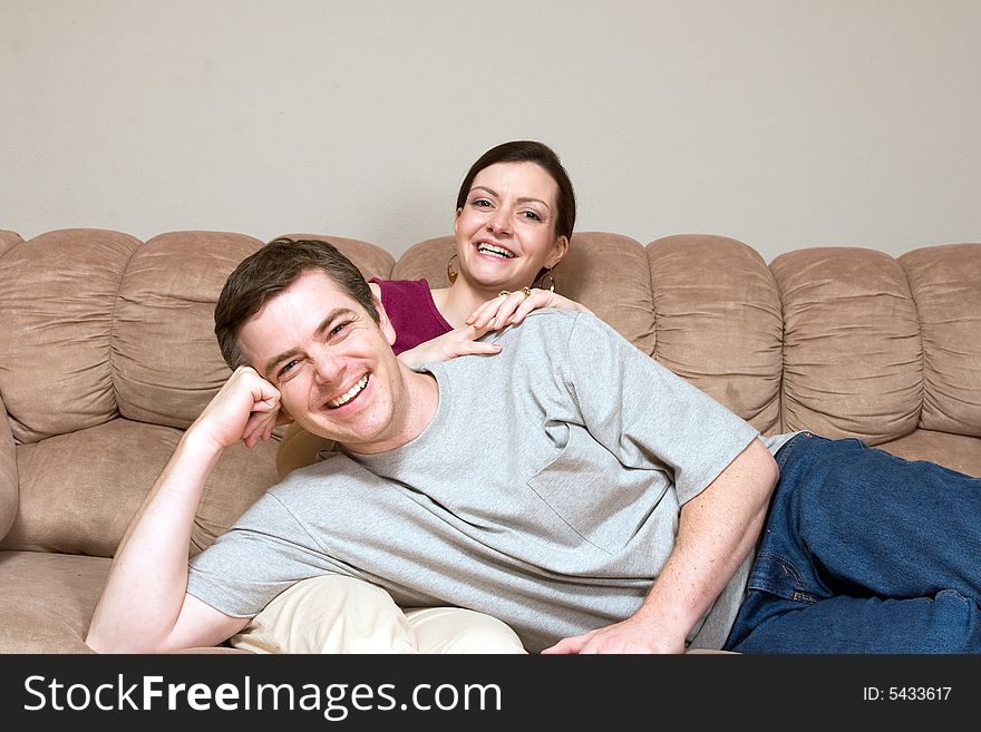 Smiling, happy couple sitting on a couch. They are laughing as he lays across her lap. Horizontally framed photograph. Smiling, happy couple sitting on a couch. They are laughing as he lays across her lap. Horizontally framed photograph