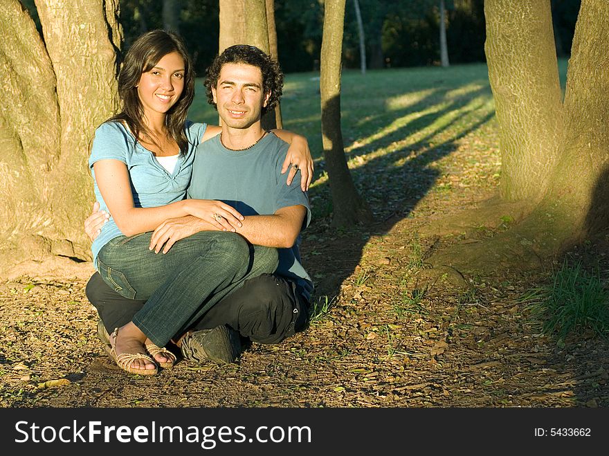 Happy, attractive couple sit in the woods. She sits on his lap a they both smile. Horizontally framed photograph. Happy, attractive couple sit in the woods. She sits on his lap a they both smile. Horizontally framed photograph