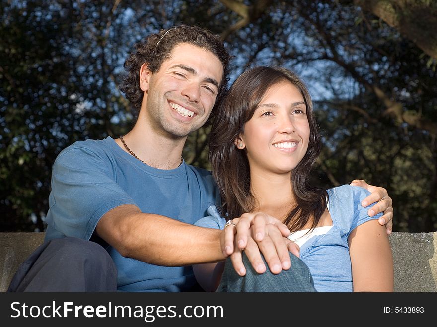 Portrait of a happy couple sitting on a bench. They are smiling and clasping hands. Portrait of a happy couple sitting on a bench. They are smiling and clasping hands