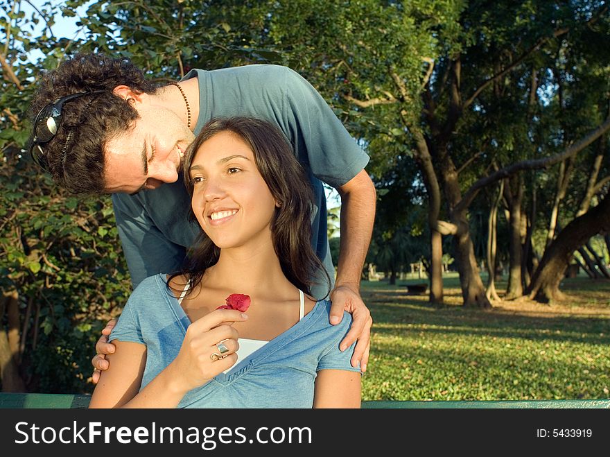 A man kisses his girlfriend's head as she smiles holding a red flower. Horizontally framed photograph. A man kisses his girlfriend's head as she smiles holding a red flower. Horizontally framed photograph.
