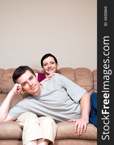 Smiling, happy couple sitting on a couch. He lays across her lap. Vertically framed photograph. Smiling, happy couple sitting on a couch. He lays across her lap. Vertically framed photograph