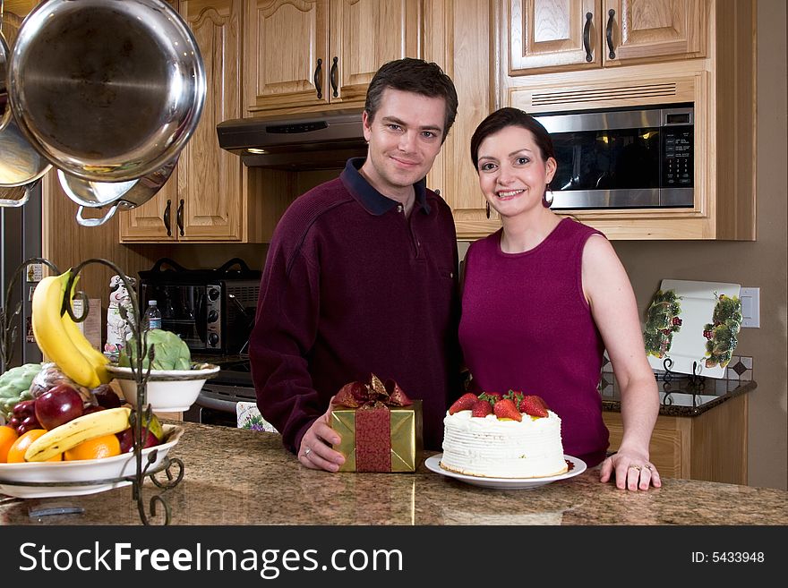 Happy couple in a kitchen with a neutral expression on their faces. He is holding a present. Horizontally framed photograph. Happy couple in a kitchen with a neutral expression on their faces. He is holding a present. Horizontally framed photograph.