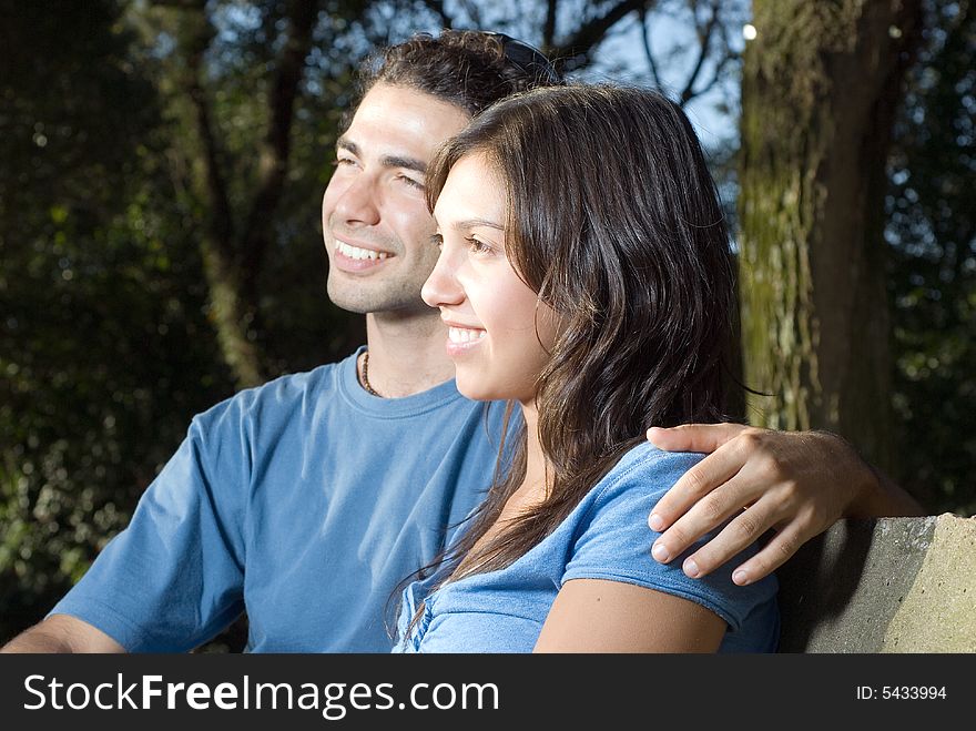 Couple smiling into the distance as they sit with their arms around each other on a stone bench. Horizontally framed photograph. Couple smiling into the distance as they sit with their arms around each other on a stone bench. Horizontally framed photograph.