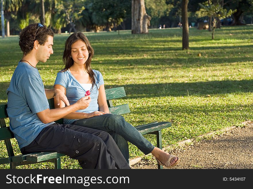 Couple sitting on a park bench looking at a red flower. Horizontally framed photograph. Couple sitting on a park bench looking at a red flower. Horizontally framed photograph.