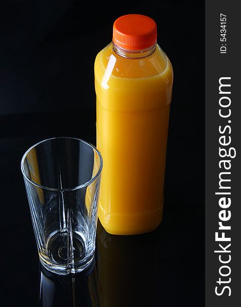 Fresh orange juice in a bottle, standing next to a empty glass, shot on black