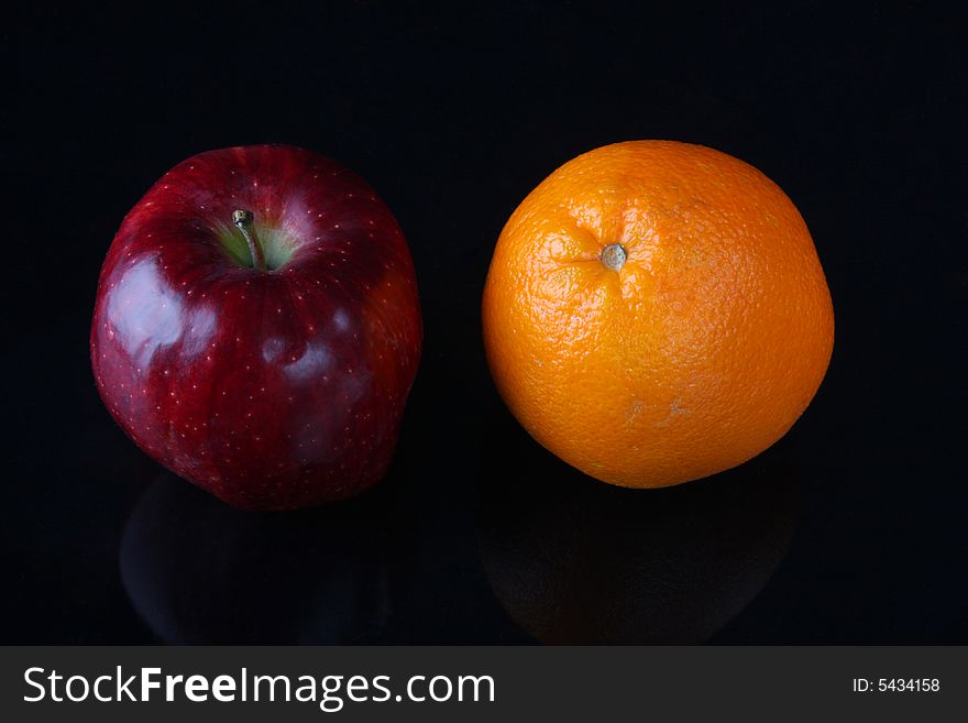 Red apple and orange side by side, shot in studio on black background