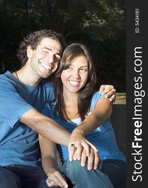 Happy, attractive couple sit in a park. They are smiling and embracing each other. Vertically framed photograph. Happy, attractive couple sit in a park. They are smiling and embracing each other. Vertically framed photograph