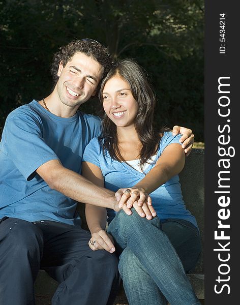 Portrait of a happy couple sitting on a bench. They are smiling and clasping hands. Portrait of a happy couple sitting on a bench. They are smiling and clasping hands