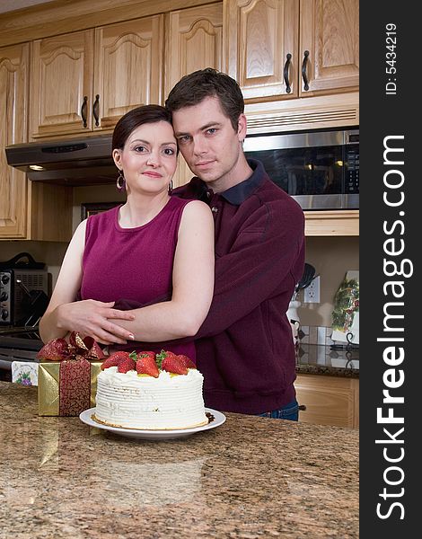 Happy couple hugging in a kitchen near a cake and a present. Vertically framed photograph. Happy couple hugging in a kitchen near a cake and a present. Vertically framed photograph.