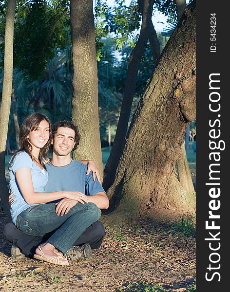 Happy, attractive couple sit in the woods. She sits on his lap a they both smile. Vertically framed photograph. Happy, attractive couple sit in the woods. She sits on his lap a they both smile. Vertically framed photograph