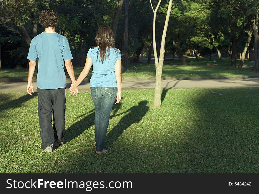 Couple holds hands as they walk through a park. Horizontally framed photograph. Couple holds hands as they walk through a park. Horizontally framed photograph.
