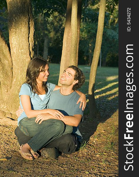 Happy, couple sit in the woods. She sits on his lap as he looks up at the sky. Vertically framed photograph. Happy, couple sit in the woods. She sits on his lap as he looks up at the sky. Vertically framed photograph