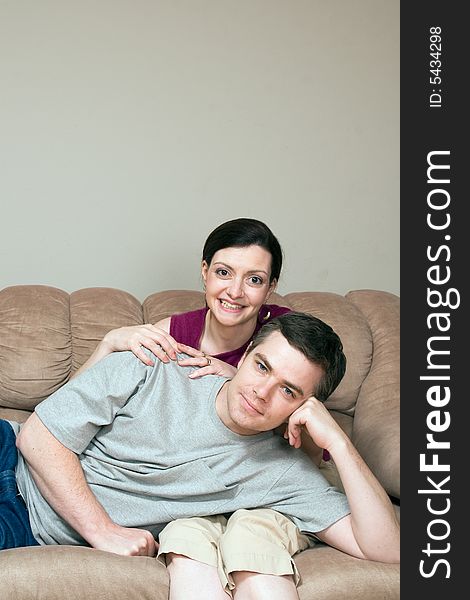 Smiling, happy couple sitting on a couch. He lays across her lap. Vertically framed photograph. Smiling, happy couple sitting on a couch. He lays across her lap. Vertically framed photograph