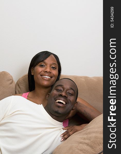 Happy, smiling, attractive couple on a couch. He is lying across her lap, laughing. Vertically framed photograph. Happy, smiling, attractive couple on a couch. He is lying across her lap, laughing. Vertically framed photograph