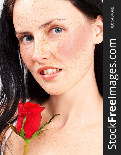 Portrait of a beautiful brunette woman with light grey eyes and freckles on her skin. She is holding a single red rose. Portrait of a beautiful brunette woman with light grey eyes and freckles on her skin. She is holding a single red rose