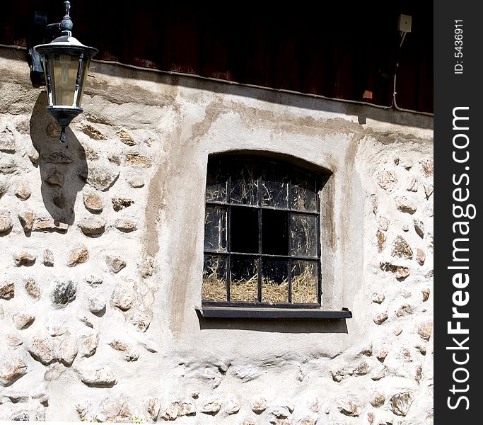 Old stony stable wall with a black window and a nice lamp. Old stony stable wall with a black window and a nice lamp