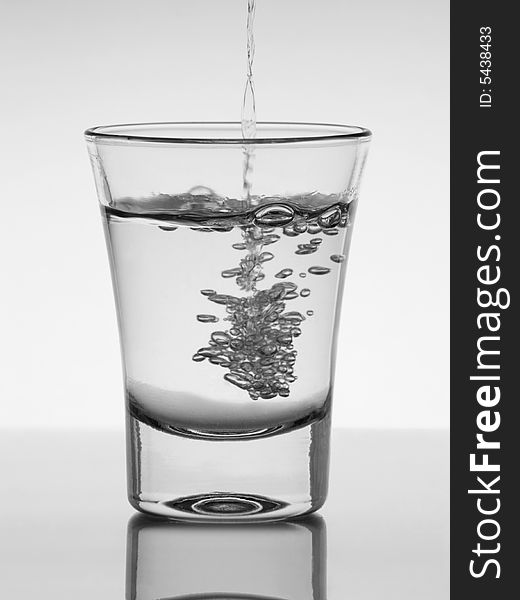Water being poured into a glass with reflection on white background. Water being poured into a glass with reflection on white background.