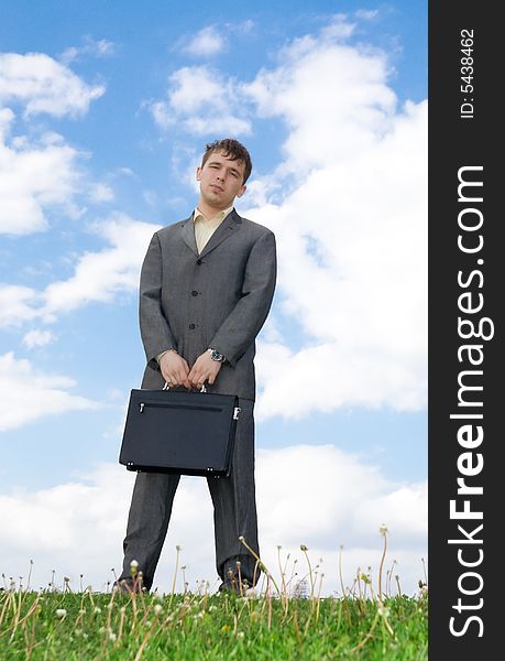 The young businessman with the handbag standing on a green grass. The young businessman with the handbag standing on a green grass