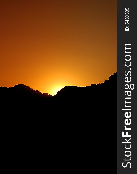 A stunning orange sun setting behind the silhouette of a craggy mountain in the Arizona desert-this shot is available in horizontal and vertical formats. A stunning orange sun setting behind the silhouette of a craggy mountain in the Arizona desert-this shot is available in horizontal and vertical formats
