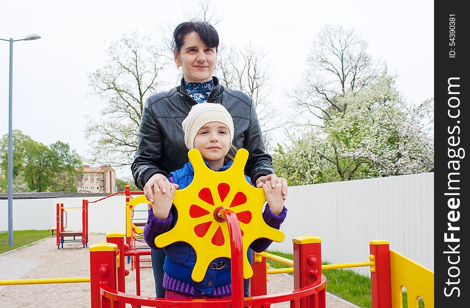 Mom plays with her daughter at the playground on a toy ship on spring day