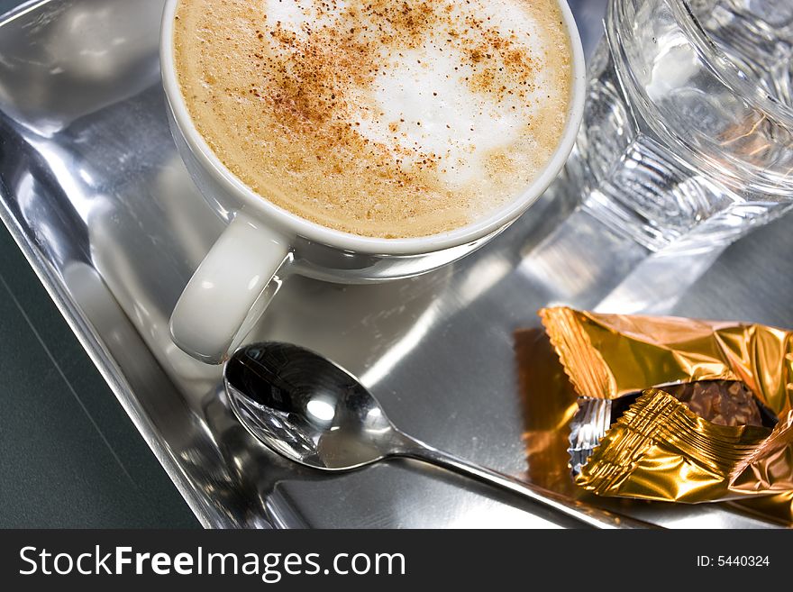 Capuccino in a white cup with chocolate and glass of water. Capuccino in a white cup with chocolate and glass of water