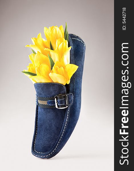 Yellow flowers stuffed in a blue leather shoe.