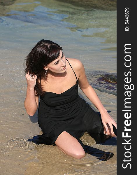 A beautiful white caucasian girl sitting in the water at the beach with her hand in her hair. A beautiful white caucasian girl sitting in the water at the beach with her hand in her hair