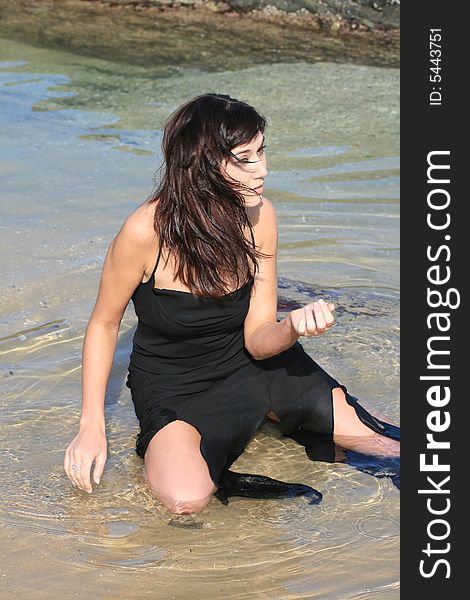 A beautiful white caucasian woman with healthy, long brunette hair sitting in the water at the beach. A beautiful white caucasian woman with healthy, long brunette hair sitting in the water at the beach