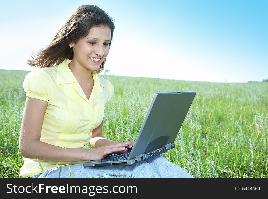 Pretty woman with laptop on the green grass under blue sky