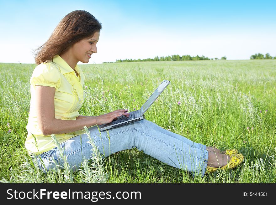 Pretty woman with laptop on the green grass