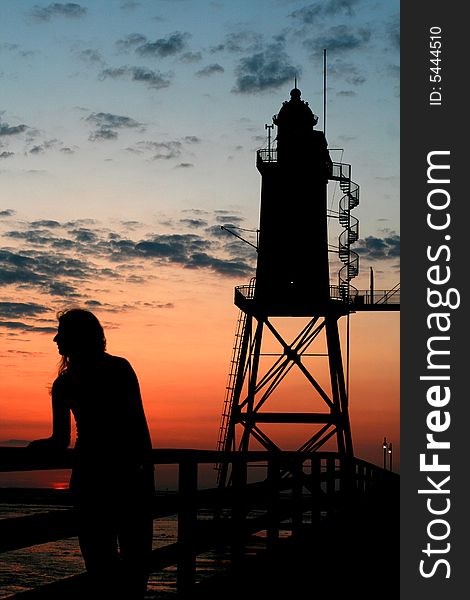 Silhouette of a girl in front of a lighthouse at sunset. Silhouette of a girl in front of a lighthouse at sunset
