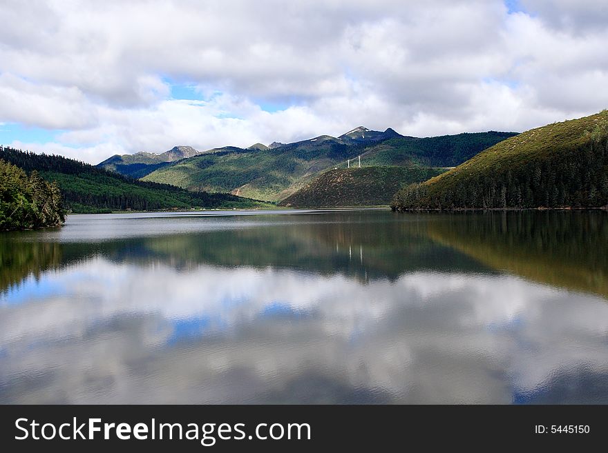 Lake in mountains surrounded by woods and the cloudy sky above it. Lake in mountains surrounded by woods and the cloudy sky above it.