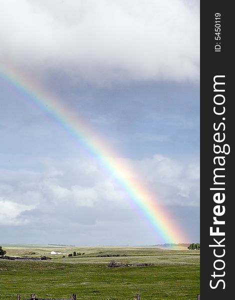 Rainbow over green pasture blue sky and clouds vertical view