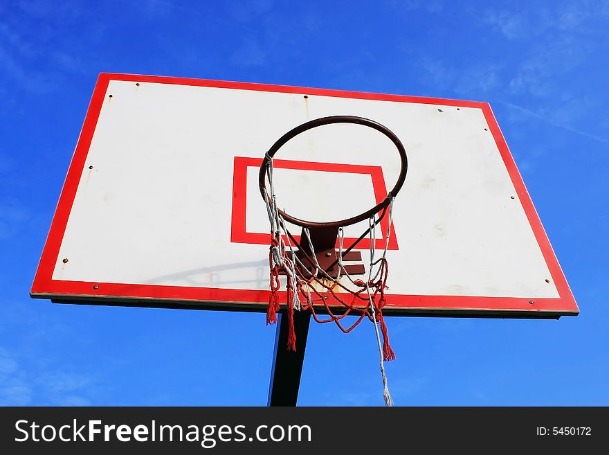 Basketball hoop with damaged net over blue sky.